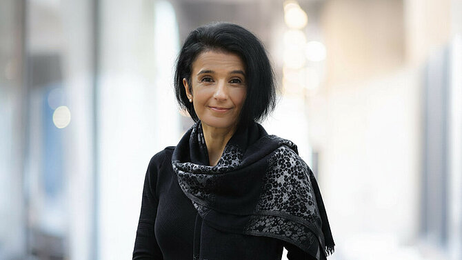 Florence Petkow in a black top and patterned scarf against a bright office background