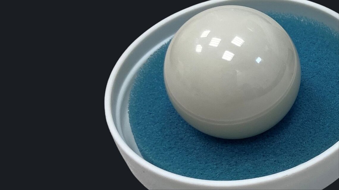 Close-up of a polished Prozyr® zirconia femoral head seated in a white bowl on a blue textured surface.