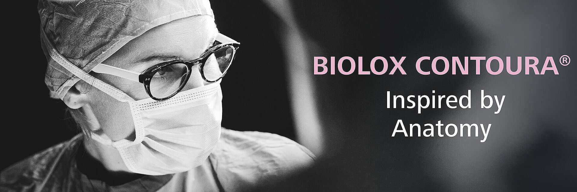 A black and white image of a female surgeon wearing glasses, scrubs and a mask