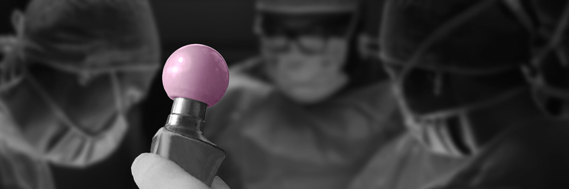 Nahaufnahme eines Chirurgen, der einen BIOLOX®delta-Keramik-Femurkopf in der Hand hält. Im Hintergrund bereiten sich drei Mitglieder des Operationsteams auf eine Hüfttotalendoprothes Operation vor. Das Bild unterstreicht den Einsatz moderner keramischer Biomaterialien in der orthopädischen Gelenkersatzchirurgie.
