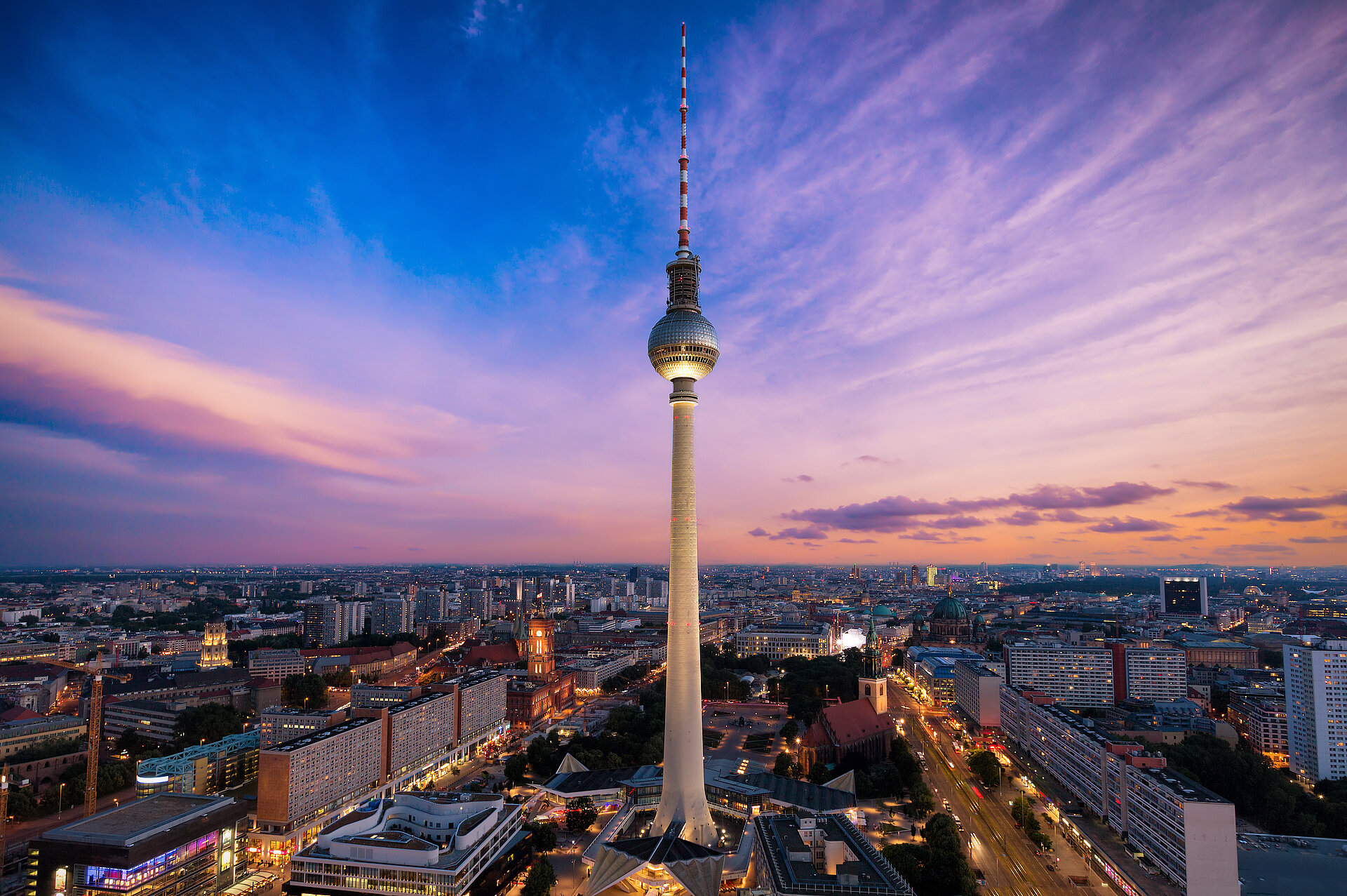 Berlin Television Tower rising above the city skyline at sunset.
