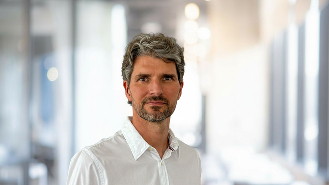 Alessandro Alan Porporati im weißen Hemd vor einem hellen, weich unscharfen Büroflur