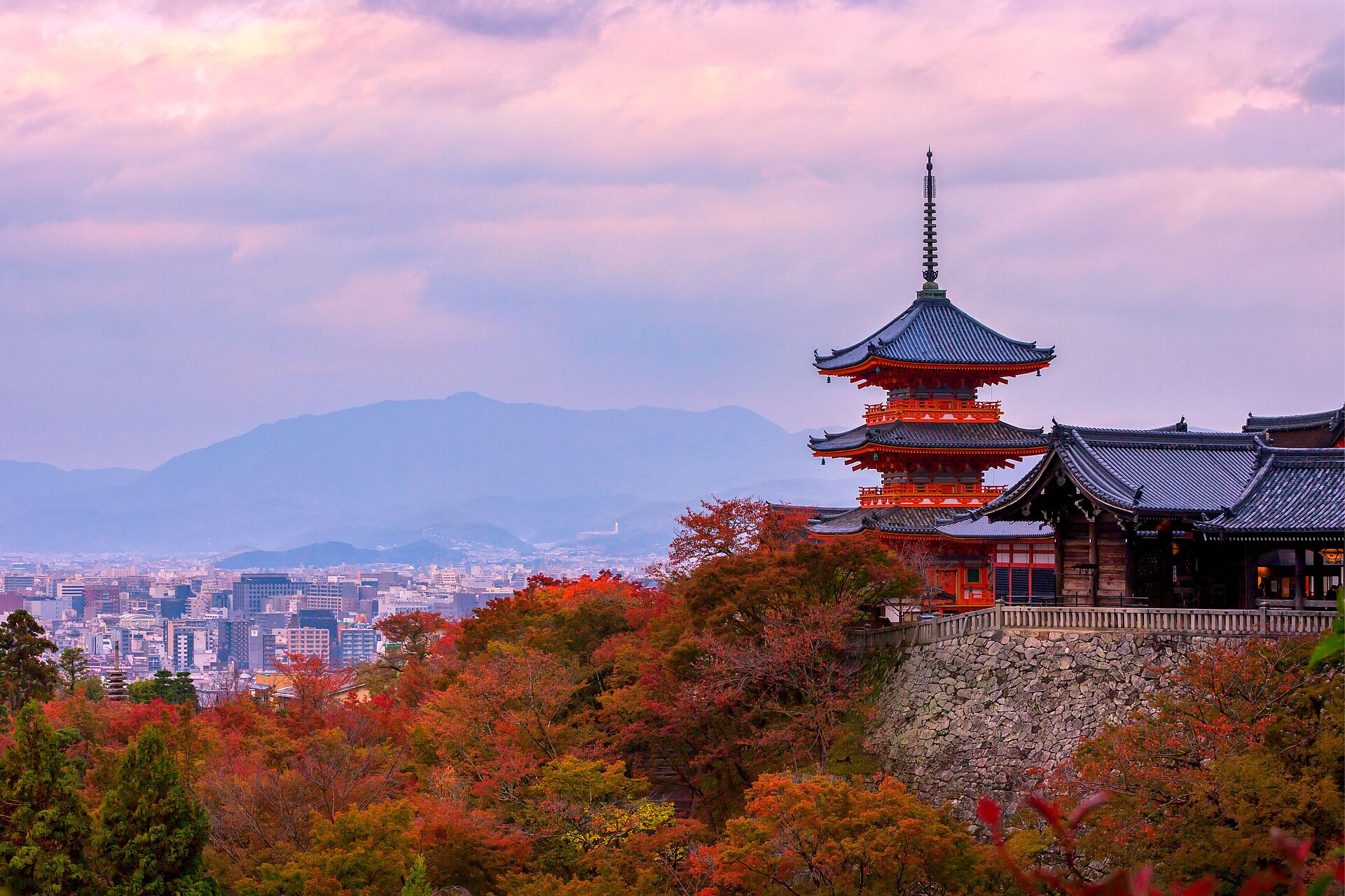 Kyoto temple overlooking the city and autumn foliage beneath a pink sky.