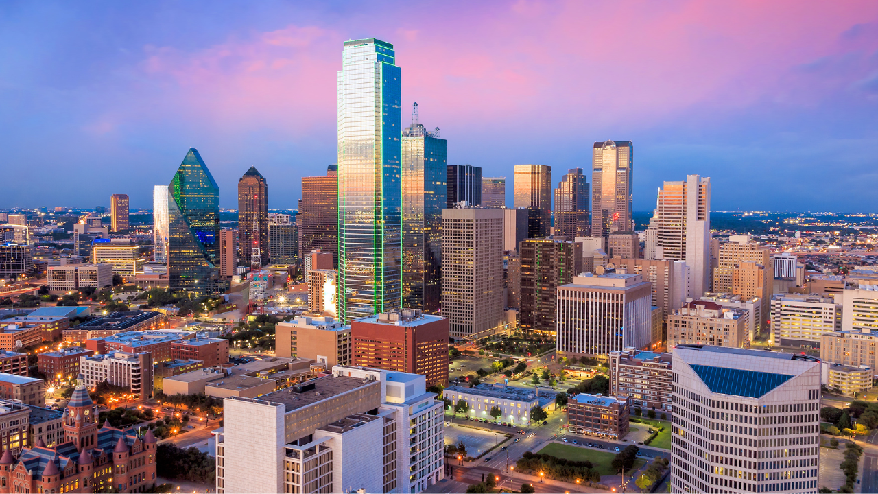 Dallas skyline at sunset with illuminated downtown skyscrapers.