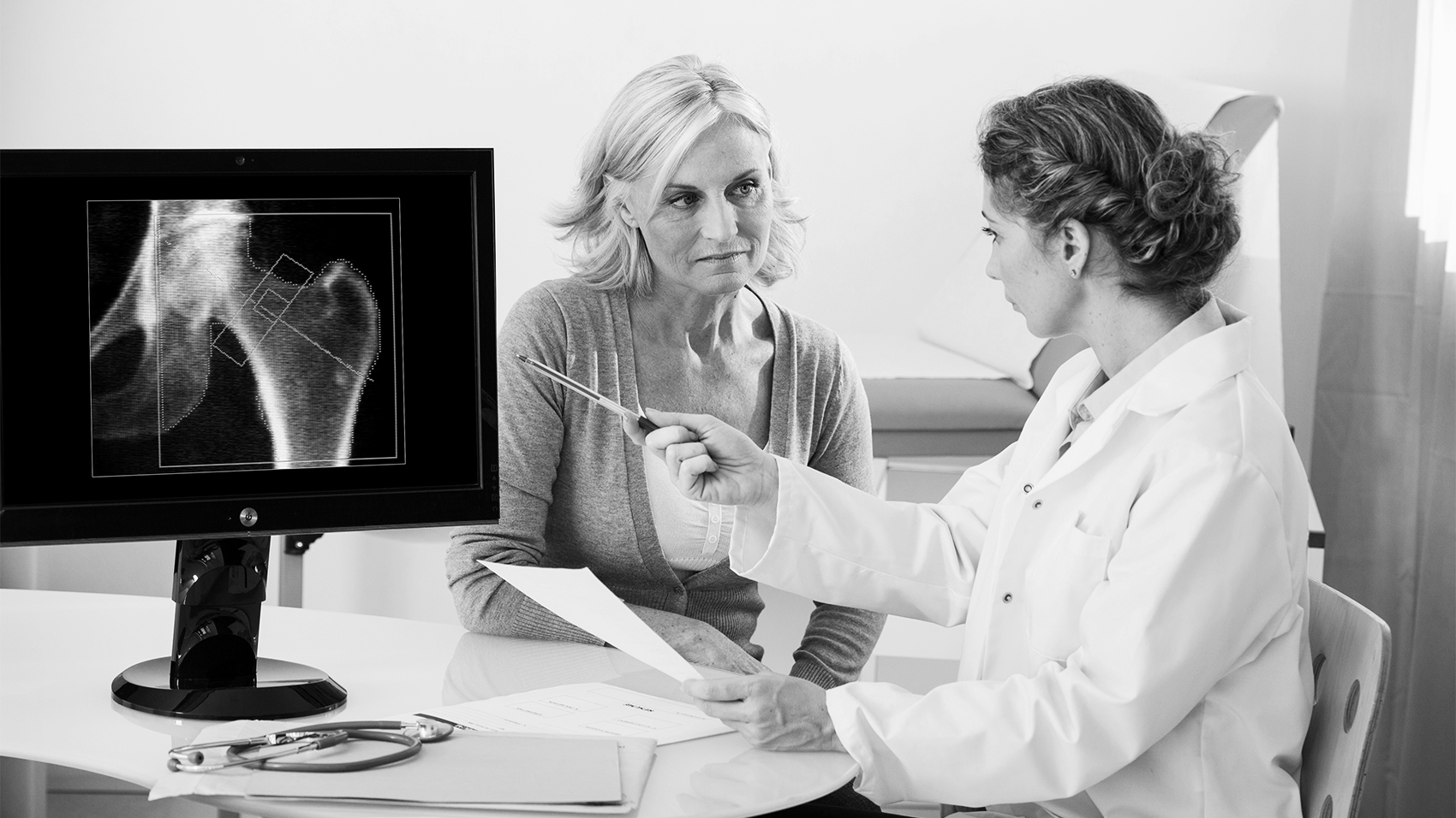 Black and white image of a female doctor and patient discussing an X-ray image of a hip